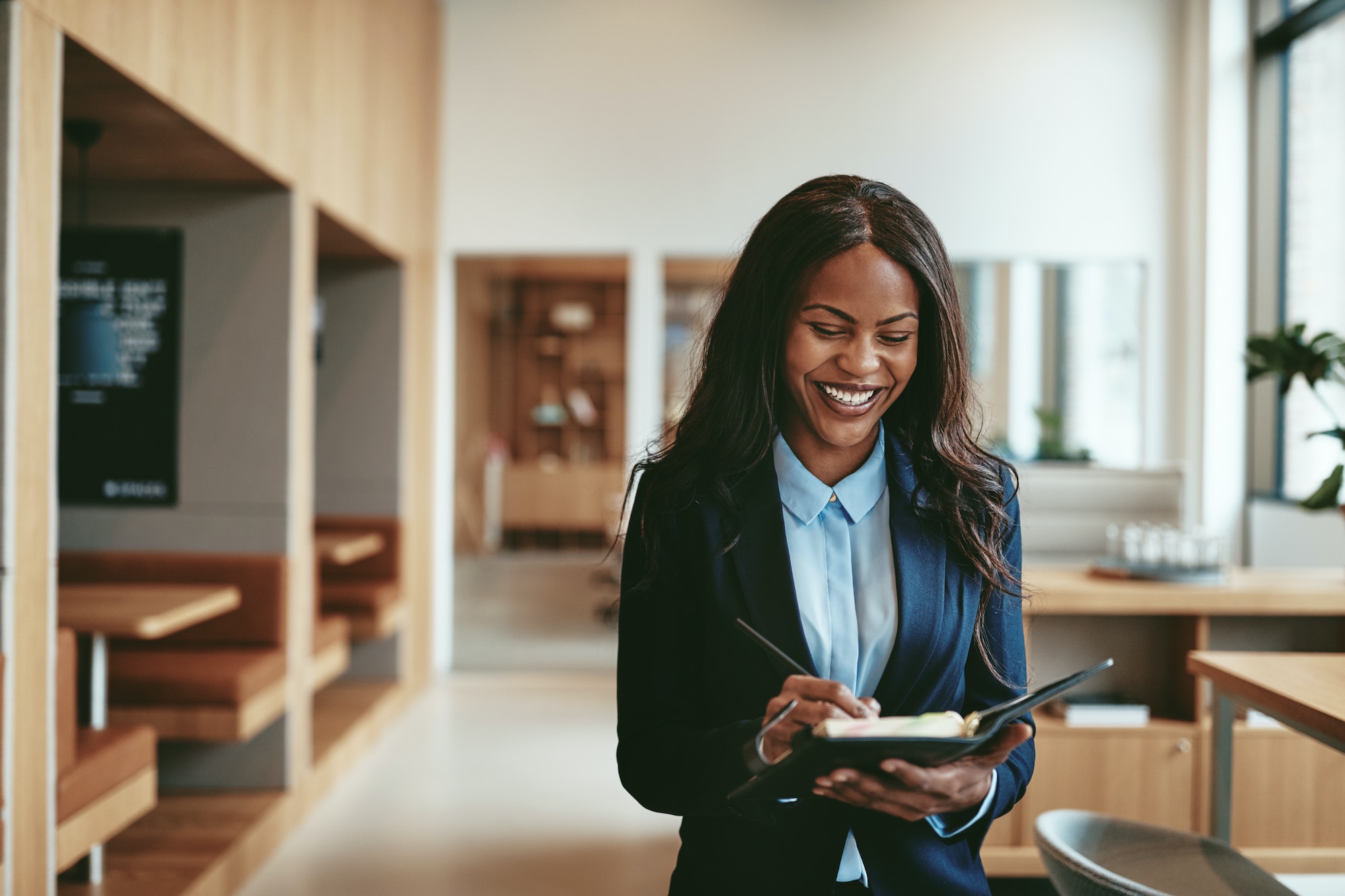 Laughing African American businesswoman walking in in office writing notes